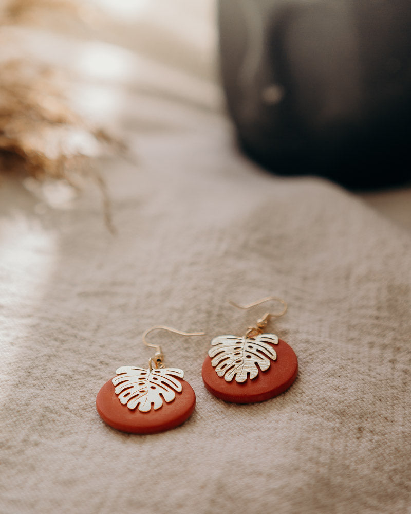 Terracotta matte disc fish hook earrings with a monstera leaf charm.